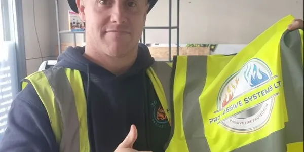 Luke from Pro Passive Systems Ltd in a hard hat, giving a thumbs up and holding up his printed hi-vis vest